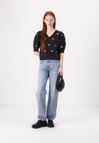 Maglione nero con scollatura a V e motivi a cuore bianchi, maniche a sbuffo; abbinato a jeans larghi blu chiaro e scarpe platform nere, mentre tiene una borsa nera.