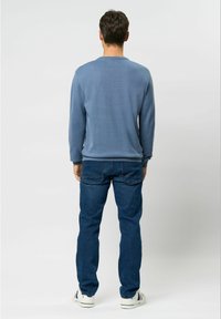 Blå langærmet pullover med en tekstureret overflade, kombineret med mørkeblå jeans. Sættet inkluderer hvide sneakers med kontraststriber.