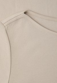 Gros plan sur un tissu beige montrant des coutures détaillées sur la couture d'épaule et l'encolure d'un vêtement.