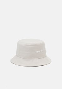 Light beige bucket hat made of soft fabric, featuring a round top and wide brim. Includes a white Nike logo on the front.