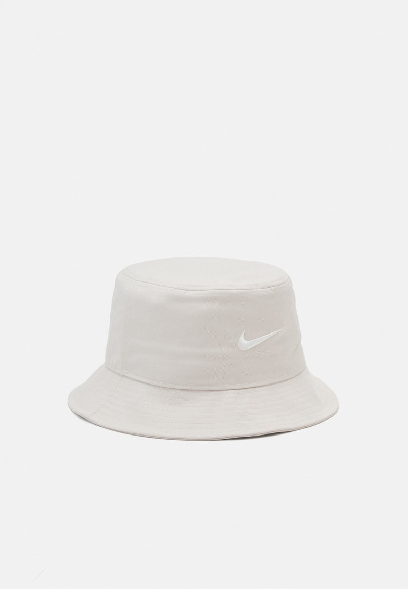 Light beige bucket hat made of soft fabric, featuring a round top and wide brim. Includes a white Nike logo on the front.