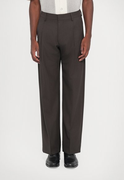 Pantalons marron foncé à taille haute et jambe droite. Fabriqués en tissu lisse, dotés de passants de ceinture et de plis marqués. Chaussures noires portées.
