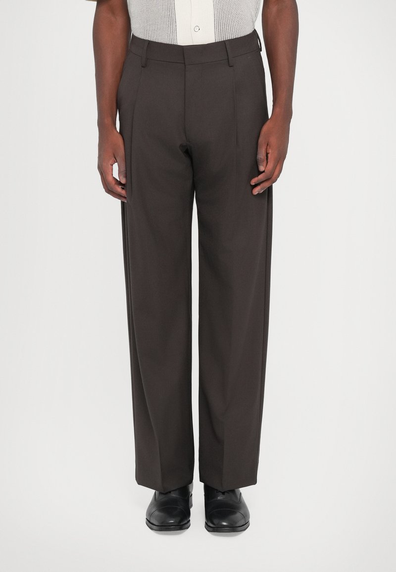 Dark brown, high-waisted trousers with a straight leg design. Made of smooth fabric, featuring belt loops and pressed creases. Black shoes worn.