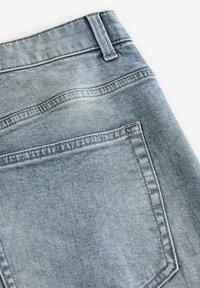 Jeans din denim bleu deschis, cu un buzunar posterior, estompare subtilă și cusături contrastante pe margini. Design clasic cu cinci buzunare.