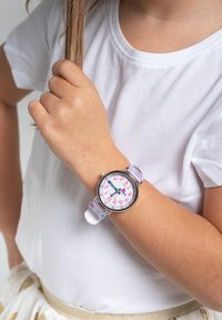 Montre pour enfants avec un bracelet en silicone rose et blanc, un boîtier rond en argent et un cadran coloré avec de grands chiffres et des cœurs.