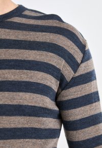 Pull rayé avec des bandes alternées de bleu marine et de beige, col côtelé et texture douce. Gros plan sur la zone de l'épaule et de la manche.