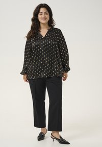 Black blouse with gold leaf pattern, collared neckline, long sleeves, paired with black trousers and pointed slingback heels. Smooth texture.