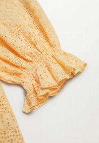 Tela de encaje amarilla con un patrón de calados, que presenta detalles fruncidos en el puño. Textura suave con un diseño fluido.