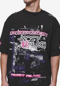 Black oversized t-shirt made of cotton, featuring colorful graphic prints in pink, purple, and white, with bold text and abstract design elements.