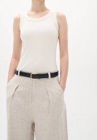 Ljust beige ribbad linne med breda axelband, kombinerat med lösa, ljusgrå linnebyxor med framfåror och ett svart bälte med guldbälte.