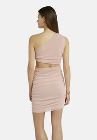 Ein schulterfreies blassrosa Kleid mit gerafftem Stoff, ausgeschnittenem Rücken und Raffung. Glatte Textur und knielanges Design. Goldschmuckakzente.