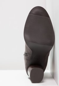 Botín de ante gris hasta el tobillo con puntera redondeada, cremallera lateral y suela de goma texturizada negra. Presenta un tacón en bloque de aspecto madera en color marrón.