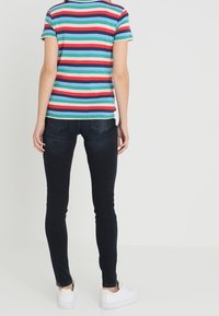 Korte mouwen, gestreept shirt in blauw, rood en groen; gecombineerd met donkere skinny jeans en witte sneakers, gezien van de achterkant.