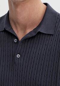 Navy textured polo shirt featuring a cable-knit pattern, a classic collar, and two button closures at the neck. Soft, knitted fabric.