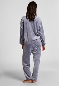 Grijze velours loungewear set met een losse pullover en broeken met elastische tailleband. Zachte textuur met lange mouwen en taps toelopende pijpen.