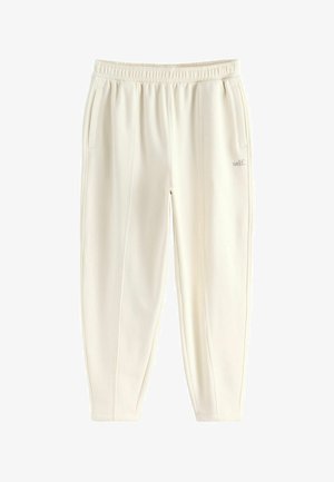 Light beige sweatpants with an elastic waistband, two side pockets, and subtle stitching detail. Fabric appears soft and textured.