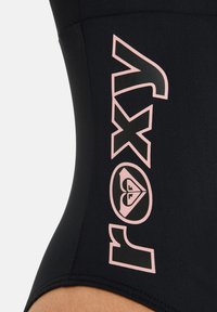 Bodysuit noir avec un grand logo "Roxy" rose et un emblème en forme de cœur. Texture lisse, design moulant, mettant en valeur la taille.