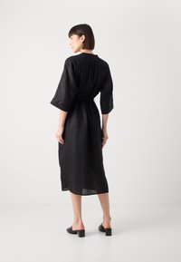 Μαύρο λινό φόρεμα με τρία τέταρτα μανίκια, στενή μέση και μήκος μέχρι το μισό μοσχάρι. Λείος υφή, απλός σχεδιασμός και ελάχιστες λεπτομέρειες.