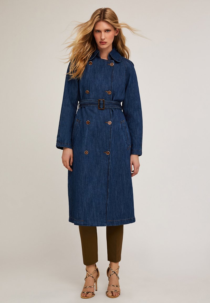 Denimowy płaszcz trench z paskiem w talii, podwójnym zapięciem i dużymi guzikami. Posiada kołnierz i boczne kieszenie. Głęboki niebieski kolor.