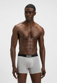 Boxer grigi con fascia elastica nera e logo "BOSS". Texture liscia, forma aderente e lunghezza a metà coscia.