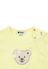 Gelbes Baumwoll-T-Shirt mit rundem Halsausschnitt, ausgestattet mit einem Plüschbären-Applikation mit einer Schleife und Druckknopfdetails an der Schulter.