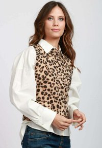 Gilet di maglina a stampa leopardata sopra una camicia bianca con bottoni, dotato di scollatura a girocollo e vestibilità rilassata. Il tessuto ha una consistenza morbida.
