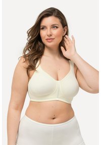 Sostenedor de color amarillo claro con tirantes anchos, textura suave y escote en forma de V. Presenta un sutil detalle de costura en la parte delantera.