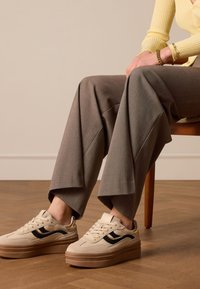 Beige platform sneakers with black stripes, paired with gray wide-leg trousers featuring a textured pattern.