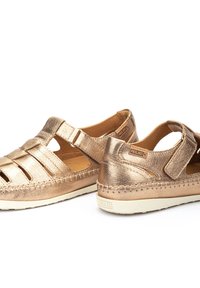 Sandalias metálicas de bronce con correa ajustable, diseño abierto, cuero texturizado y recortes geométricos. Suela de goma con detalles de costura.