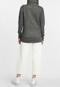 Grå stickad turtlenecktröja med långa ärmar och ribbade muddar, tillsammans med vita vida byxor och vita högskoor.