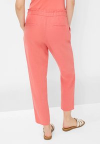 Koraalkleurige linnenmix broek met een elastische taille, twee achterzakken en rechte pijpen, gecombineerd met witte sandalen met bandjes.