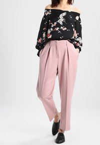 Czarny top bez ramiączek w kwiatowy wzór, zestawiony z jasnoróżowymi, wysokimi spodniami w kant oraz czarnymi, teksturowanymi mokasynami.
