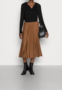 Černá mikina s dlouhým rukávem, hnědá plisovaná midi sukně, černé kotníkové boty a černá kabelka. Hladké textury a kontrastní barvy.