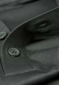 Donkergrijze button-up shirt detail met een kraag, twee ronde grijze knopen en een gladde stofstructuur met zichtbare stiksels.