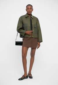 Green jacket with large pockets, black skirt, and black shoes. The jacket has a relaxed fit and gold hardware accents.