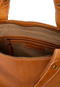Intérieur d'un sac en cuir marron avec fermeture éclair, présentant une doublure en tissu beige et une petite poche zippée. Couture renforcée le long des bords.