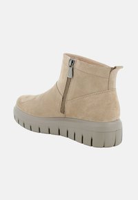 Stivali alla caviglia in suede beige con zip laterale, dotati di una suola piatta grigia chiara e suola testurizzata per una migliore aderenza.