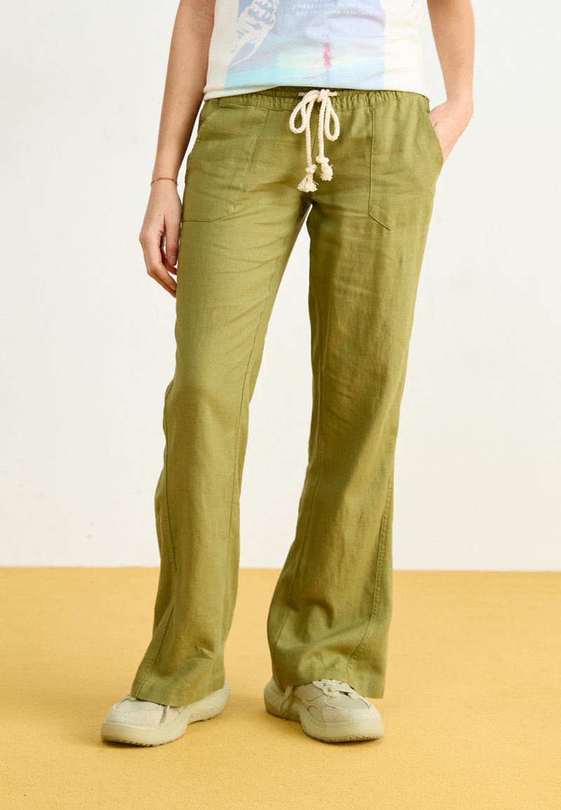 Green, loose-fitting linen pants with a drawstring waist, featuring two front pockets and a casual design. Textured fabric and neutral color.