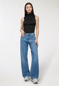 Czarny bezrękawnik z golfem połączony z jasnoniebieskimi, szerokimi dżinsami i srebrnymi sneakersami. Gładki materiał i luźny krój.