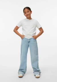 Camiseta de algodón blanca con un bolsillo decorativo, combinada con jeans de pierna ancha azul claro y zapatillas beige con acentos blancos.