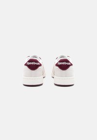 Sneakers Reebok w jasnoszarym kolorze z ciemnoczerwonymi akcentami. Górna część z gładkiej skóry, wygodny kołnierz oraz gumowa podeszwa o kontrastowej fakturze.
