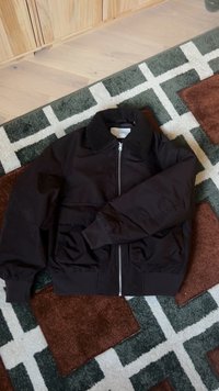 Giacca bomber nera con colletto testurizzato, chiusura con zip e due tasche frontali. Il tessuto sembra liscio con una leggera lucentezza.