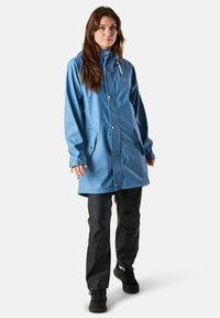 Giacca da pioggia blu impermeabile con cappuccio, chiusure a pressione e tasche laterali, abbinata a pantaloni neri impermeabili e calzature nere robuste.