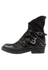 Svart läderankelstövel med slapp skaft, spännband och metallnitar. Har en rundad tå och en strukturerad bakpanel.