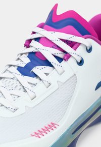 Weißer Sportschuh mit strukturiertem Obermaterial, blauen und pinken Akzenten, flachen Schnürsenkeln und einer auffälligen, sichtbaren Luftpolstersohle.