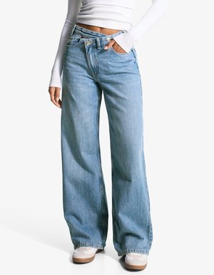 Svetle modré džíny s širšími nohavicemi, vyrobené z denimu, s vysokým pasem, předními kapsami a uvolněným střihem. Stylizované s bílými teniskami.