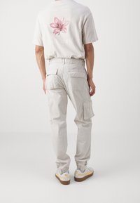 Vaaleanharmaat farkkuihin tyyliin tehdyt monitaskuiset cargo-housut, rento istuvuus ja kapeat lahkeet. Yhdistetty beigeen graafiseen t-paitaan, jossa on kukkakuosi.