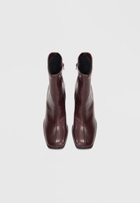 Bottines en cuir bourgogne avec une texture lisse, un bout pointu et une fermeture éclair sur le côté, présentant des détails de couture minimaux.