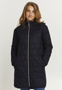 Abrigo negro acolchado con capucha, que presenta un cuello alto, cierre frontal plateado y bolsillos laterales. Patrón de ondas texturizado en la tela.