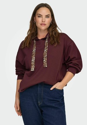 Bordo spalvos gobtuvas su leopardų rašto virvutėmis, per didelis dydis ir banguoti rankogaliai, derinamas su tamsiai mėlynomis džinsomis. Lygaus audinio tekstūra.